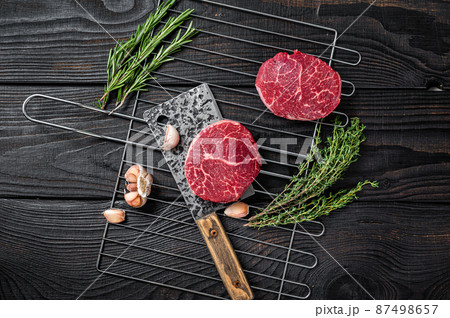 Grill BBQ - Raw Fillet Mignon beef steaks with herbs. Black wooden background. Top view Grill BBQ - Raw Fillet Mignon beef steaks with herbs. Black wooden background. Top view 87498657