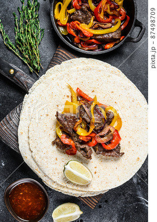 Mexican Fajitas with colored pepper and onions, served with tortillas and salsa. Black background. Top view Mexican Fajitas with colored pepper and onions, served with tortillas and salsa. Black background. Top view 87498709