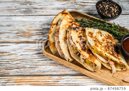 Vegetarian snacks quesadilla with vegetables and cheese on wooden tray. White wooden background. Top view. Copy space Vegetarian snacks quesadilla with vegetables and cheese on wooden tray. White wooden background. Top view. Copy space 87498759