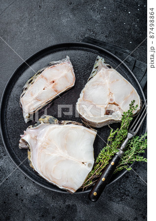 Fresh Raw wolffish o wolf fish Steak on a plate. Black background. Top view 87498864