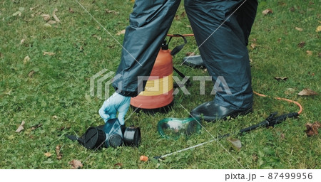 Lawn treatment with insecticides and toxins from ixodic mites and other blood sucking parasites. A man in a protective suit sprays poison on the grass 87499956