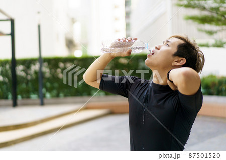 Active Asian sportsman relaxing and drinking a water in bottle after outdoor running or workout. Asian man drink a water during the break from exercise. A healthy man trying hard for cardio workout. 87501520