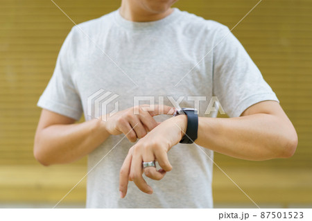 Active Asian young sportsman using a smartwatch or smart fitness band to track his outdoor workout and activities, man reviewing an exercise and health information after finished outdoor workout. 87501523