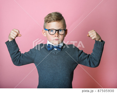 Confident kid boy shows muscles. Sport child boy showing his hand biceps muscles strength. School pupil in glasses. Nerd smart kid isolated on pink background. Back to school Confident kid boy shows muscles. Sport child boy showing his hand biceps muscles strength. School pupil in glasses. Nerd smart kid isolated on pink background. Back to school 87505930