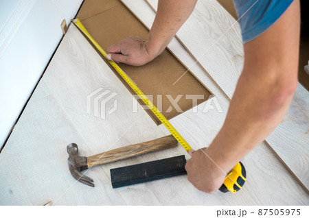 Man hands with ruler and hammer. Man installing new laminate white floor. Several of laminated panels 87505975