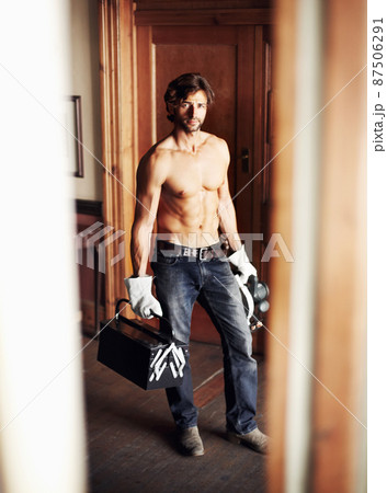 Where would you like me to start. Attractive young handyman standing shirtless while holding his tools. 87506291