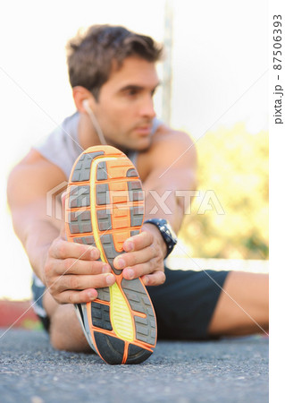 Stretching those muscles before a jog. Young jogger sitting and stretching while looking sideways. 87506393