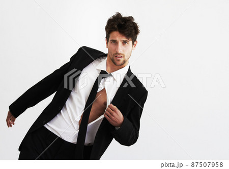 He has that effect on ladies. Portrait of a sexy young man pulling open his unbuttoned shirt wearing a smart balck suit and tie - Copyspace. 87507958