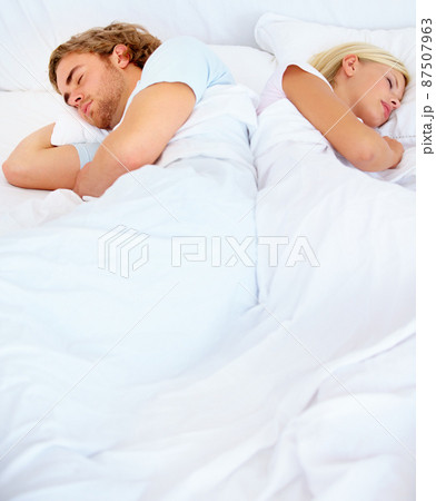 At odds with one another. A young couple sleeping back to back in bed. At odds with one another. A young couple sleeping back to back in bed. 87507963