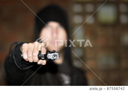 Criminal in control. View of a man holding a gun and pointing at you. 87508742