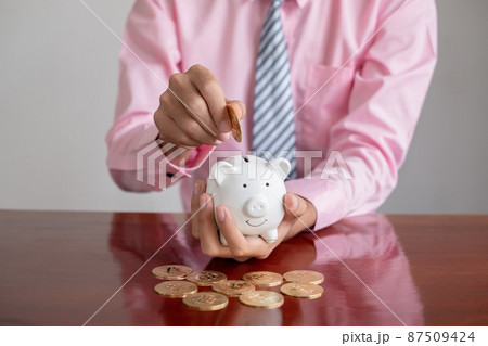 The hand of a businessman puts coins in a piggy bank, saves money with coins, steps into a successful growth business, and saves for retirement concept The hand of a businessman puts coins in a piggy bank, saves money with coins, steps into a successful growth business, and saves for retirement concept 87509424