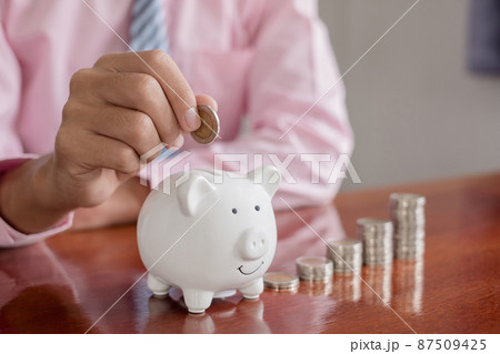 The hand of a businessman puts coins in a piggy bank, saves money with coins, steps into a successful growth business, and saves for retirement concept 87509425