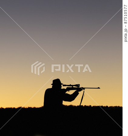 Preparing to shoot. A silhouette of a man in the outdoors holding up his sniper rifle. 87510577