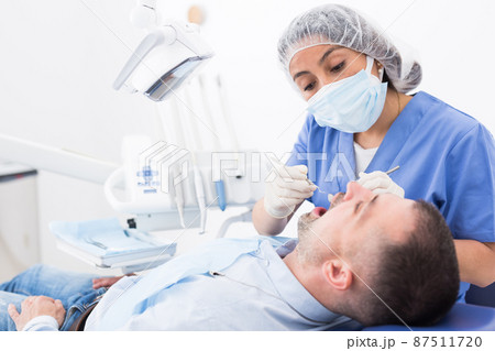 Female dentist in face mask with male patient Female dentist in face mask with male patient 87511720