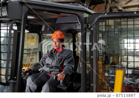 Constructor in hardhat and workwear sitting in cab of construction machine 87513897
