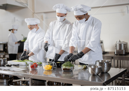 Chefs in face masks prepare takeaway food in professional kitchen Chefs in face masks prepare takeaway food in professional kitchen 87515153