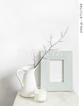 White still life. Scented candle and empty photo frame mockup on marble table. Vase with branch. 87517568