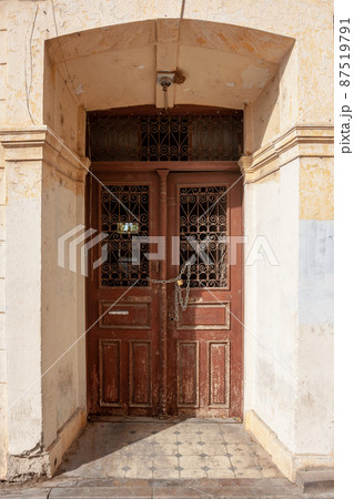 Old front door with grate closed by chain and lock in deep stone opening. Vertical photo. 87519791