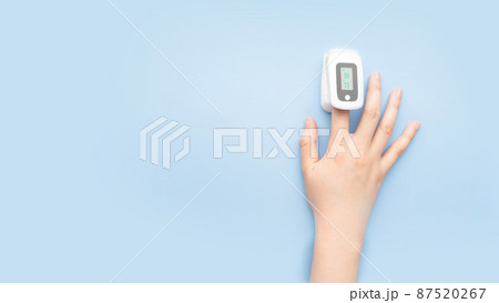 Woman using pulse oximeter finger digital device to measure oxygen saturation in blood and pulse rate on blue background. Monitor health of people with pneumonia, anemia or heart failure. 87520267