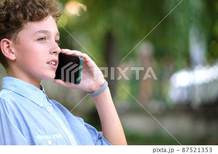 Young puzzled child boy talking on cellphone outdoors in summer park Young puzzled child boy talking on cellphone outdoors in summer park 87521353