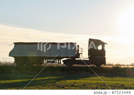 Semi-truck with tipping cargo trailer transporting sand from quarry driving on highway hauling goods in evening. Delivery transportation and logistics concept Semi-truck with tipping cargo trailer transporting sand from quarry driving on highway hauling goods in evening. Delivery transportation and logistics concept 87521449