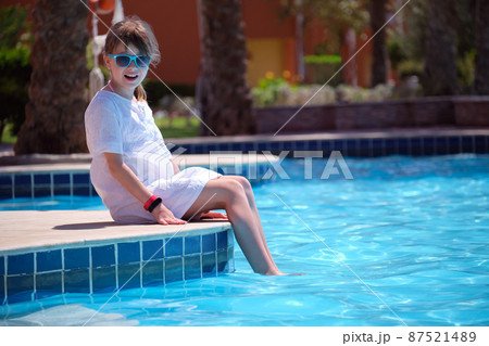 Portrait of happy child girl in white dress relaxing on swimming pool side on sunny summer day during tropical holidays 87521489