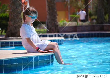 Happy child girl in white dress relaxing on swimming pool side on sunny summer day 87521732
