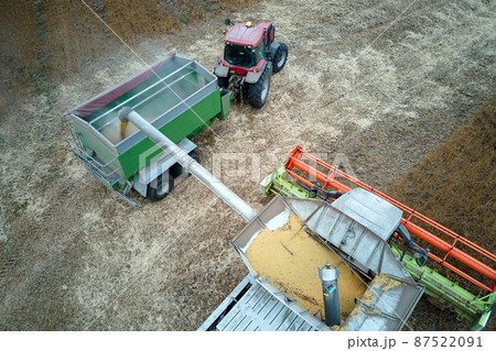 Aerial view of combine harvester unloading grain in cargo trailer working during harvesting season on large ripe wheat field. Agriculture and transportation of raw farm products concept Aerial view of combine harvester unloading grain in cargo trailer working during harvesting season on large ripe wheat field. Agriculture and transportation of raw farm products concept 87522091