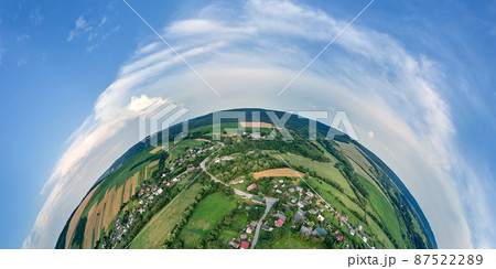 Aerial view from high altitude of little planet earth with small village houses and distant green cultivated agricultural fields with growing crops on bright summer day 87522289