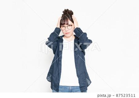 白い背景の前に立って頭痛に悩むジェスチャーをする眼鏡をかけている女性 白い背景の前に立って頭痛に悩むジェスチャーをする眼鏡をかけている女性 87523511
