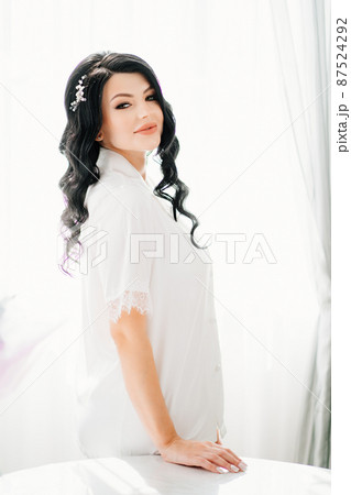 beautiful pregnant bride brunette in white pajamas by the window. beautiful pregnant bride brunette in white pajamas by the window. 87524292