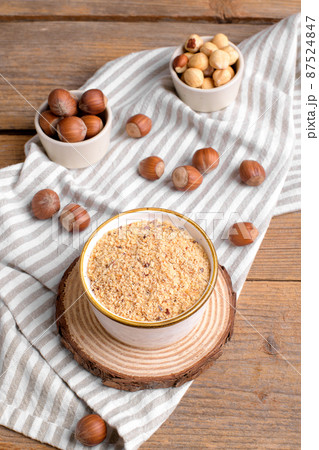 Raw Organic Ground Hazelnut Flour in a Bowl with whole nuts on rustic wooden background. Alternative nut flour 87524847