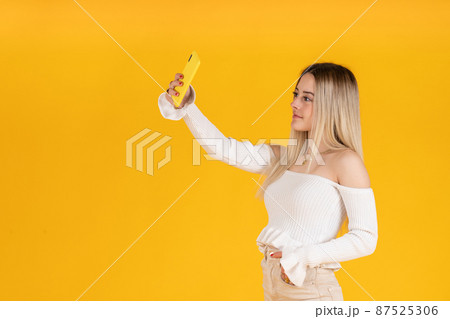 young woman taking a selfie with her smartphone. Studio photography 87525306