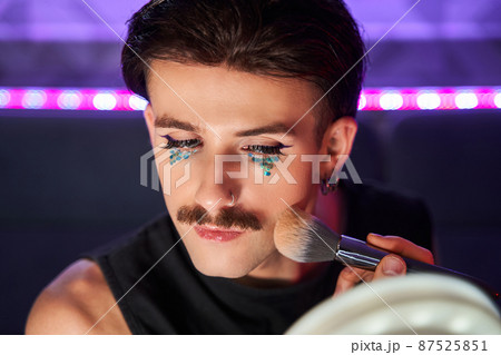 Feminine man applying blushes at his chicks with concentrated face 87525851