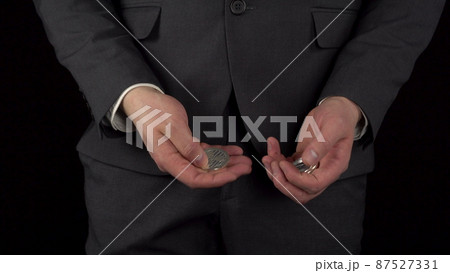 A young businessman in a suit takes out cryptocurrency coins from his pocket and recounts. The waist of a man close-up on a black background. 87527331