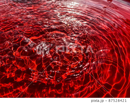 Close-up rain drips on a red background and leaves circles on the water. 87528421