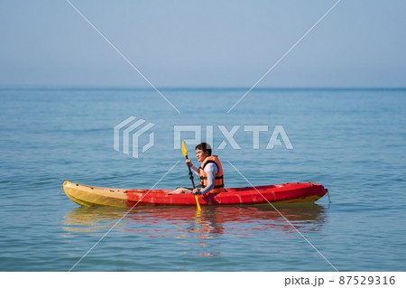 man in life jacket paddling a kayak boat in sea 87529316