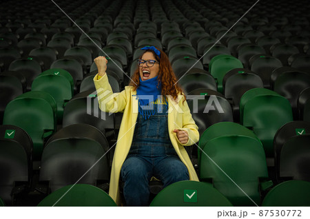 Caucasian woman cheers for a sports team at the stadium. The girl watches the match at the stadium alone. 87530772