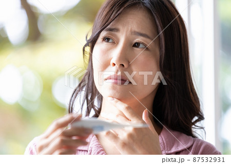手に持った体温計を見てネガティブな表情になる部屋着の女性 手に持った体温計を見てネガティブな表情になる部屋着の女性 87532931