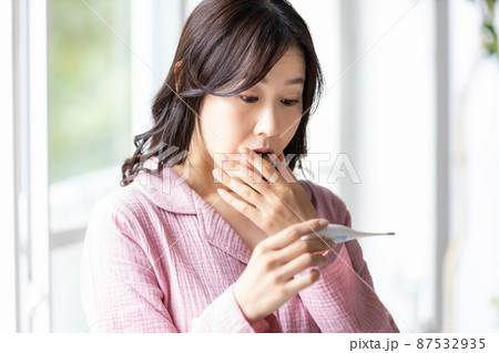 手に持った体温計を見てネガティブな表情になる部屋着の女性 87532935