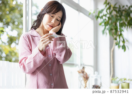 手に持った体温計を見てネガティブな表情になる部屋着の女性 手に持った体温計を見てネガティブな表情になる部屋着の女性 87532941