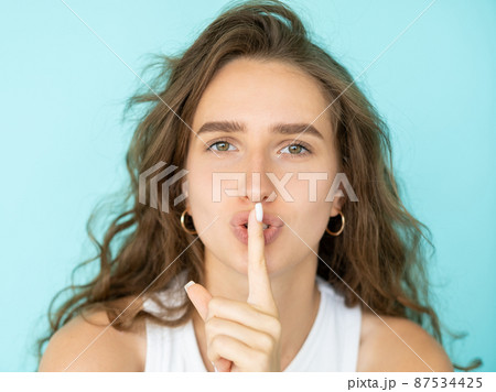 Shush finger. Female portrait. Mute expression. Pretty beautiful woman showing gesture for keeping secret isolated blue. 87534425
