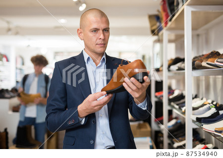 Focused man looking at brown leather dress shoe in store 87534940
