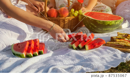 Woman takes slice of watermelon on blanket at family picnic Woman takes slice of watermelon on blanket at family picnic 87535067