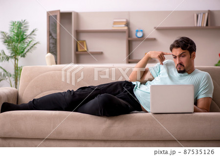 Young man sitting on the sofa with computer at home Young man sitting on the sofa with computer at home 87535126