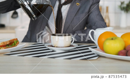 Close-up of Man Entrepreneur Pouring Coffee while Having Breakfast at Home. Coffee Spills over the Rim of the Cup. Business, Lifestyle, Overworking Concept 87535473