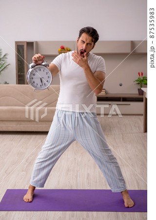 Young man doing sport exercises at home in time management conce 87535983