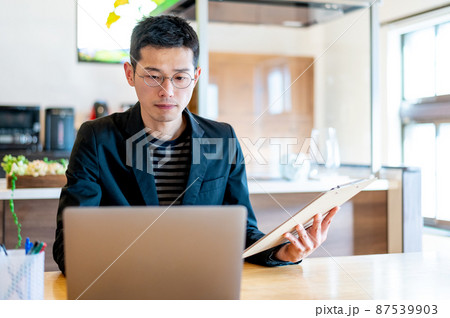 印刷した資料の内容をチェックしながらパソコン内で修正する男性起業家 87539903