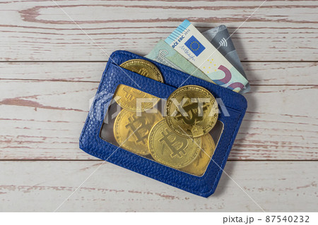Blue leather wallet with Bitcoin coins, Euro bills and bank card. Wooden background. Close-up. Top view. Blue leather wallet with Bitcoin coins, Euro bills and bank card. Wooden background. Close-up. Top view. 87540232