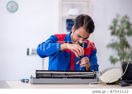 Young male repairman repairing air-conditioner Young male repairman repairing air-conditioner 87541112